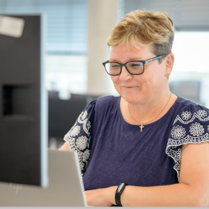 A smiling woman looks down at her computer screen